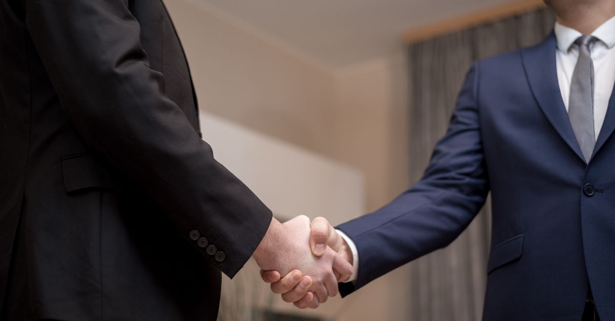 Two businessmen in suits shaking hands, emphasizing trust and partnership indoors.